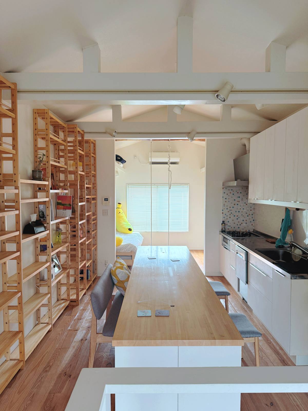 The great room — long table, shelves and kitchen in warm light.